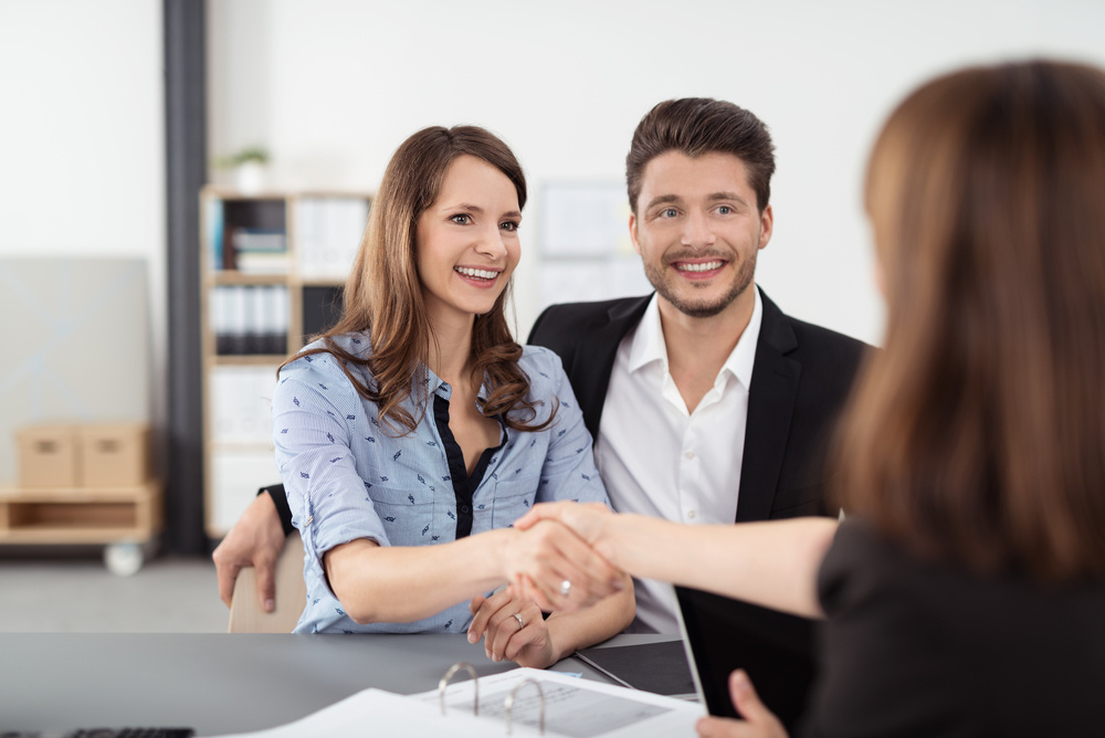 Happy Young Professional Couple Shaking Hands with a Real Estate Agent After Some Business Discussions Inside the Office.